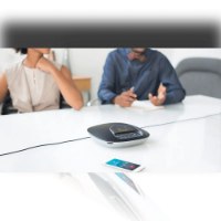 מערכת ועידה Logitech Group – יחידת רמקול כנסים שחורה וכסופה על שולחן לבן טלפון סלולרי ואנשים ברקע עם אלחוטי