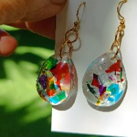 Handcrafted silver hoop earrings featuring a yellow oval resin charm with red spots and a shiny red round bead on a white background