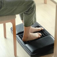 הדום ארגונומי דו צדדי ועיסוי לכפות הרגליים Comfort – אדם יושב ורגליו היחפות מונחות על משטח העיסוי השחור של ההדום
