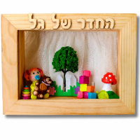 שלט כניסה ממוסגר בעץ בעבודת יד עם הכיתוב הגיל הרך. מציג דיורמה מיניאטורית של גן ילדים עם ילדה, דובון, עץ, קוביות ופטרייה אדומה. רקע וילון תחרה.