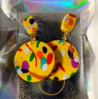 arge round pop-art polymer clay earrings in bright yellow with colorful abstract patterns, shown on a model and close-up on packaging.