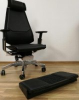 הדום ארגונומי דו צדדי ועיסוי לכפות הרגליים Comfort – הדום שחור עם משטח עילי גלי מונח על רצפת עץ ליד כיסא משרדי שחור