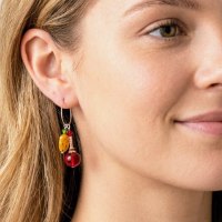 Handcrafted silver hoop earrings featuring a yellow oval resin charm with red spots and a shiny red round bead on a white background