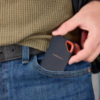 כונן SSD נייד SanDisk Extreme Portable Ssd V3 1TB – כונן SSD כחול כהה עם לולאה כתומה מוכנס לכיס ג ינס קדמי Type-C