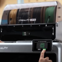 מדפסת תלת מימד Creality K2 Pro Combo – יחידת CFS עם סלילי פילמנט ואצבע לוחצת על מסך המגע