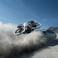 רחפן (DJI Avata 360(DJI RC 2 – רחפן אפור-לבן טס נמוך ליד מכונית המעלה אבק