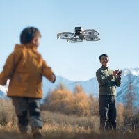 רחפן DJI Flip Fly More Combo – אדם מטיס מכשיר מעופף אפור בשדה מול הרים מושלגים