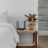 ראוטר TP-Link Archer C54 AC1200 Dual Band Wi-Fi Router – ראוטר שחור עם אנטנות על שידת עץ לצד מיטה לבנה חוטי