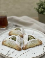 אוזן המן מבצק פריך זהוב במילוי קרם פיסטוק ירוק בוהק ושוקולד לבן.