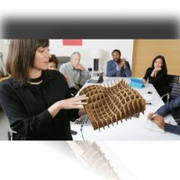 מערכת ועידה Logitech Group – חוטי אישה מציגה מודל קרטון מורכב לקבוצת עובדים יושבים סביב שולחן