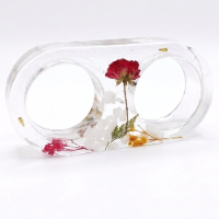 Handcrafted double oval clear resin candlestick filled with dried botanical flowers and white pebbles, holding two lit tea light candles
