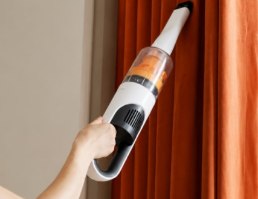 שואב אבק אלחוטי Deerma T10W – יד אוחזת בשואב אבק לבן עם מיכל אבק כתום ושואבת וילון כתום