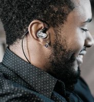 אוזניות מקצועיות מבודדות רעש Shure AONIC 4 – אוזנייה שקופה אחת מונחת באוזנו הימנית של גבר מחייך
