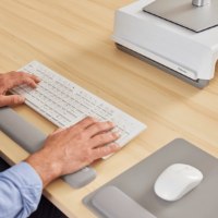 כרית יד Breyta Keyboard Wrist Rest – אדם מקליד על מקלדת לבנה מעל כרית יד אפורה