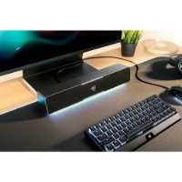 סאונדבר Razer Leviathan V2X – פריט בודד ממוקם מתחת למסך מחשב ומואר בתאורת לד כחולה לצד מקלדת ועכבר גיימינג