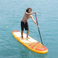 גלשן סאפ מתנפח Aqua Marina Fusion BT-26FUP – גבר עומד על גלשן סאפ צהוב וכתום וחתירה במים כחולים עם משוט