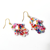 Handcrafted clear resin Hamsa earring filled with colorful mini sprinkles and a heart cutout, worn on a woman's ear.