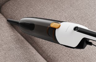 שואב אבק קומפקטי Deerma DX170 – המכשיר לבן ושחור עם מיכל שקוף מונח על בד ספה חום