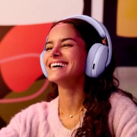 אוזניות אלחוטיות צבע סגול לילך Logitech G325 – אישה מחייכת ומרכיבה פריט שמע סגול-לילך