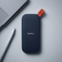 כונן חיצוני SanDisk Portable Ssd 1TB – כונן כחול כהה עם לולאה כתומה מונח לצד עט סטיילוס אפור