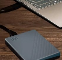 כונן קשיח חיצוני Western Digital WDBY3J0060BGY My Passport 6TB USB-C – פריט בודד בצבע אפור-כחלחל מחובר למחשב נייד על שולחן