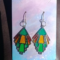 Handcrafted geometric resin dangle earring in a stained glass style with green, yellow, and red colors, casting a colorful light reflection on a woman's neck.
