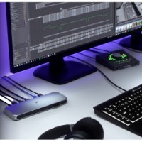 תחנת עגינה Corsair TBT100 Thunderbolt 3 Dock – התחנה הכסופה מחוברת עם כבלים על שולחן עבודה מואר לצד מסך ומחשב נייד