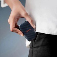 כונן SSD נייד SanDisk E10 1TB – יד מכניסה את הכונן הכחול-כהה עם לוגו SanDisk אדום לכיס מכנסיים שחורים עם USB